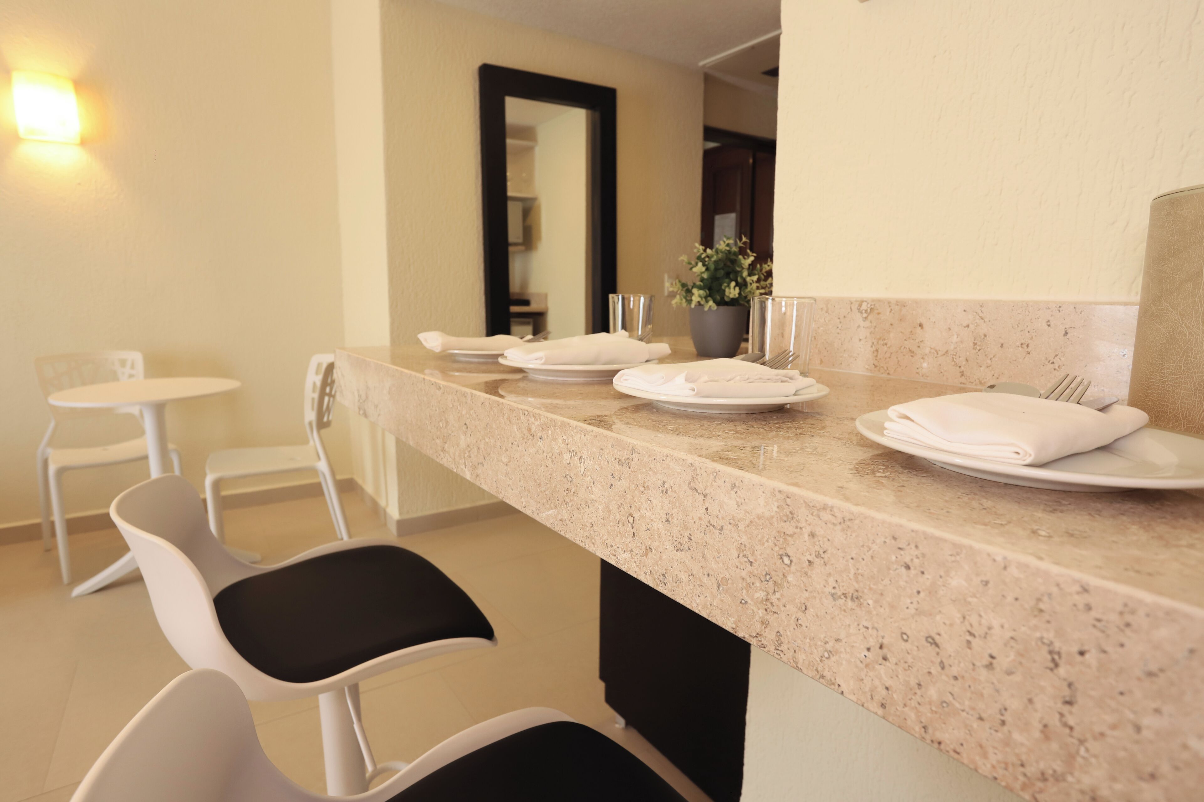 A hotel dining area with a long counter, white chairs, and a potted plant.