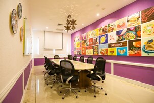 Una sala conferenze con un lungo tavolo, sedie e una parete colorata a tema gastronomico.
