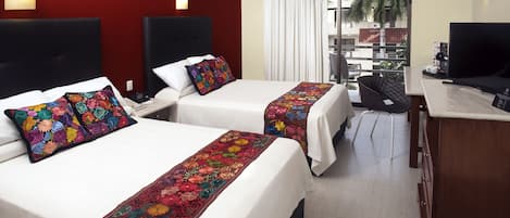 A hotel room with two beds, a desk, a television, and a view of the outside.