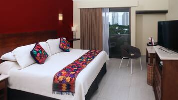Quarto de hotel com uma cama grande, uma mesa de escritório com televisão e vista para prédios pela janela.