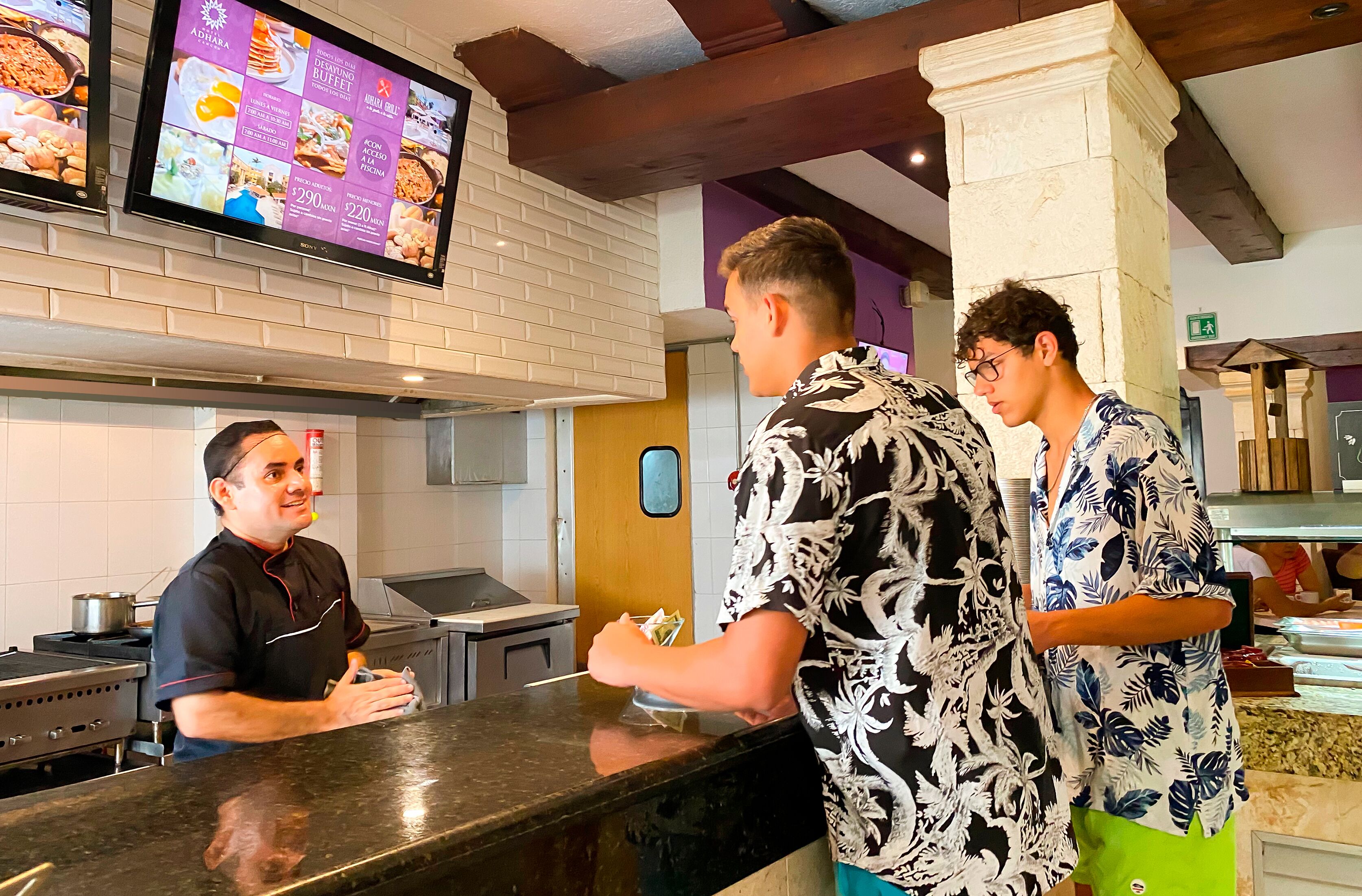 A restaurant interior with a counter, menu display, and kitchen area.