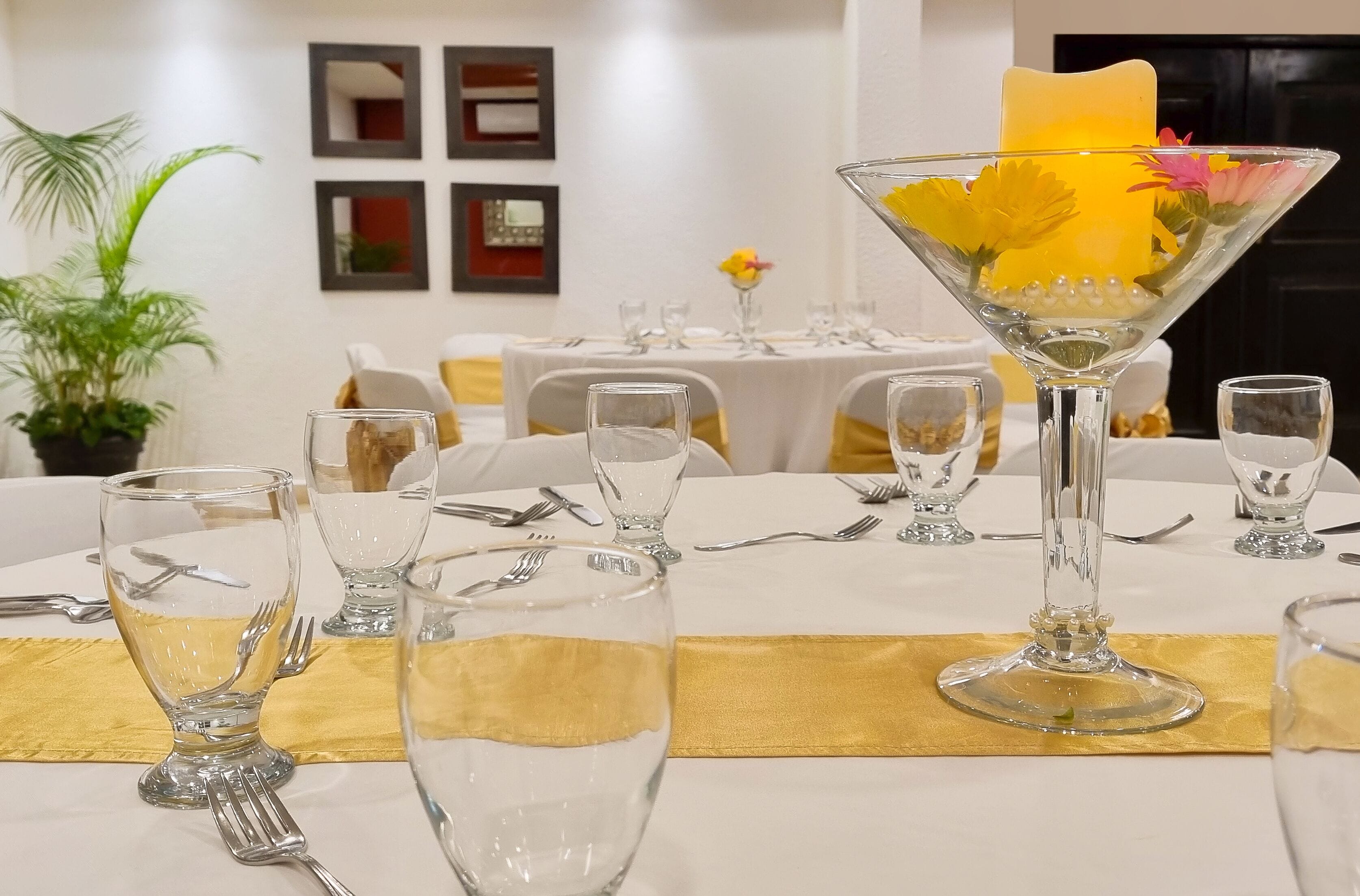 A dining table set with clear glassware, a yellow candle, and a decorative glass centerpiece.