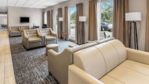 A hotel lobby with leather sofas, a flat-screen TV, and large windows with curtains.