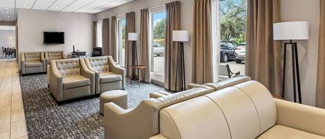 Un hall de hotel con sofás de cuero, un televisor de pantalla plana y ventanas amplias con cortinas.