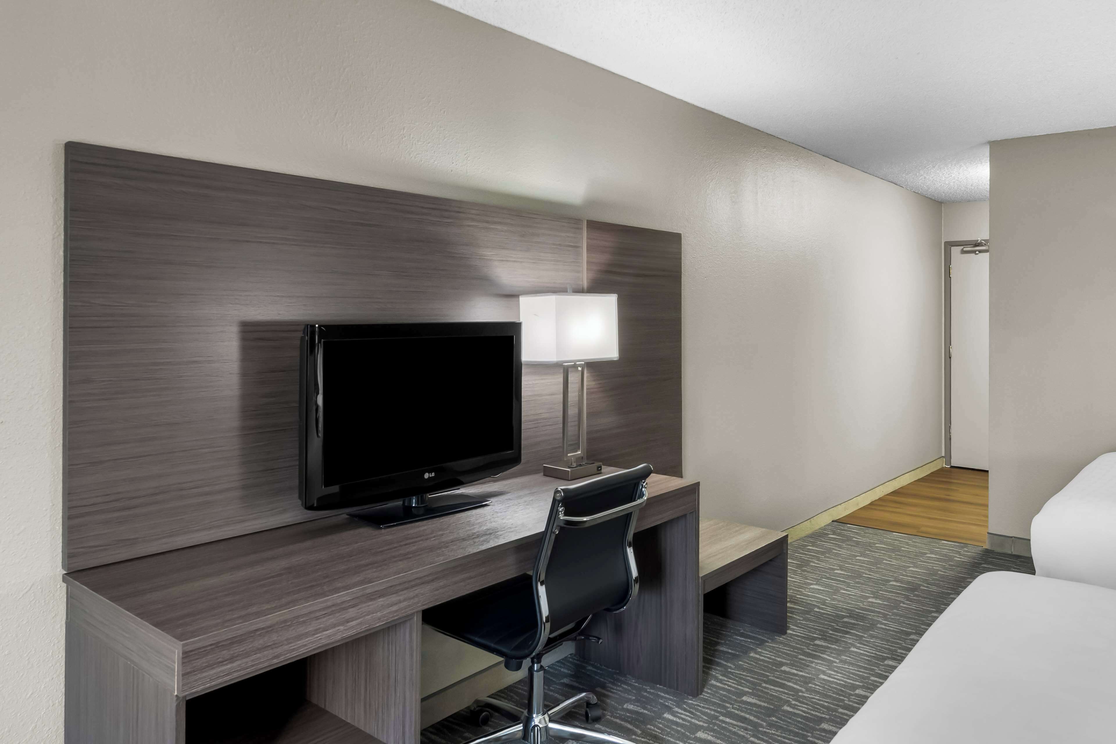 Habitación de hotel con televisión de pantalla plana, escritorio con lámpara, silla de oficina negra y cama.
