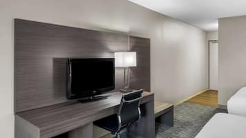 Habitación de hotel con televisión de pantalla plana, escritorio con lámpara, silla de oficina negra y cama.