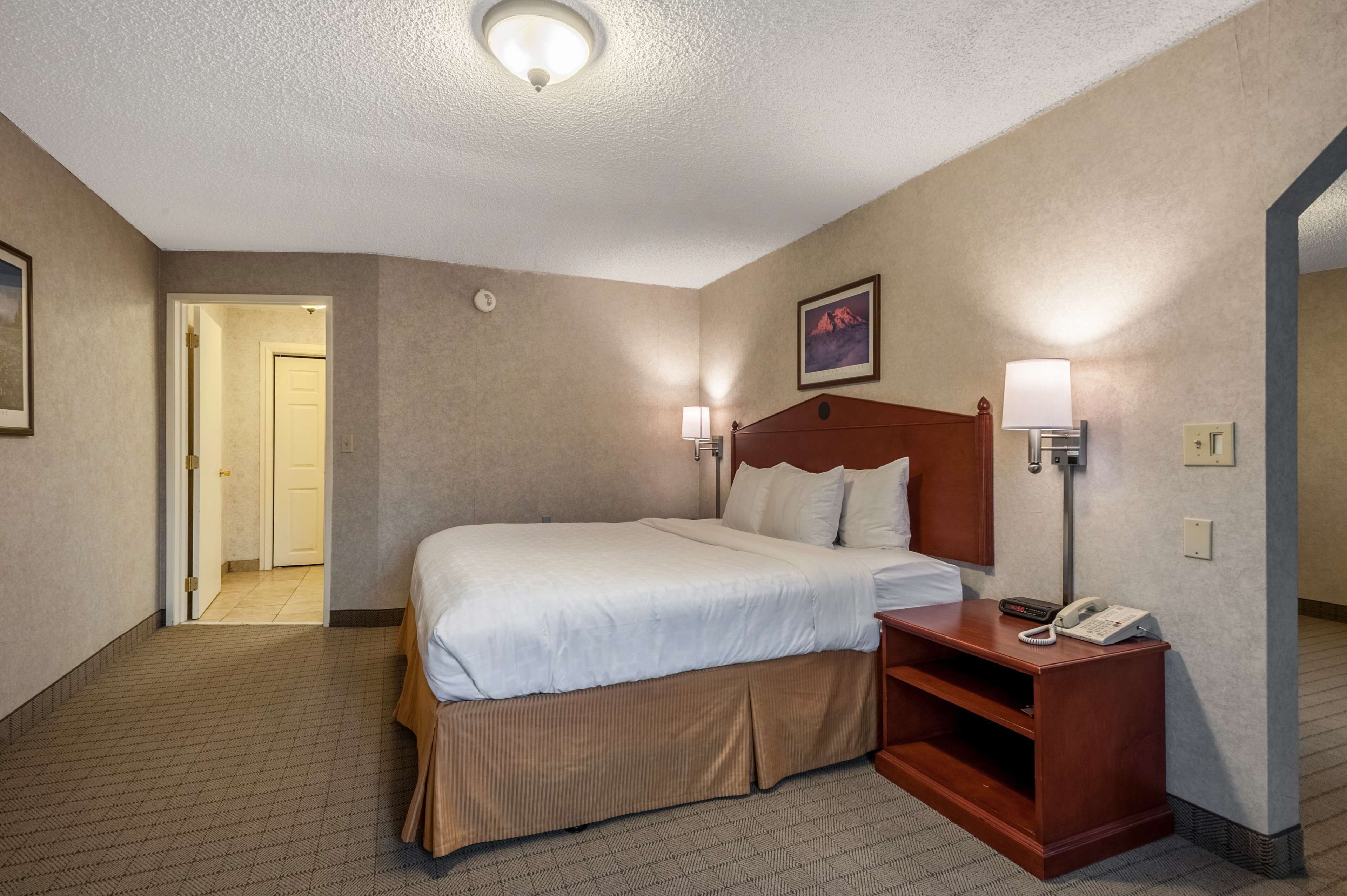 A hotel room with a large bed, bedside lamps, a wooden nightstand, and a telephone.