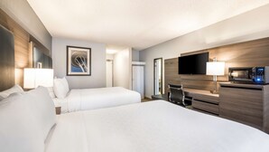 A hotel room with two beds, a TV, a microwave, and a desk with a lamp.