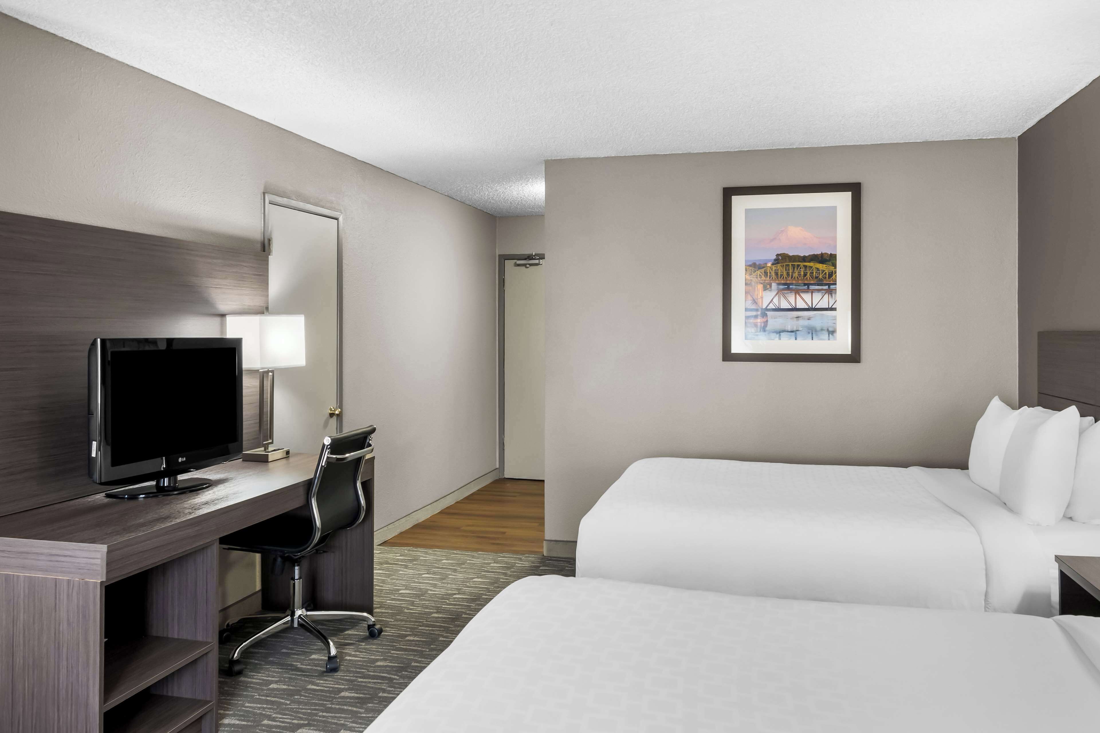 A hotel room with a bed, a desk with a computer, a chair, and a framed picture on the wall.
