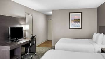 A hotel room with a bed, a desk with a computer, a chair, and a framed picture on the wall.