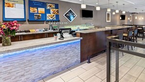 A modern breakfast area with a counter, menu boards, and seating.