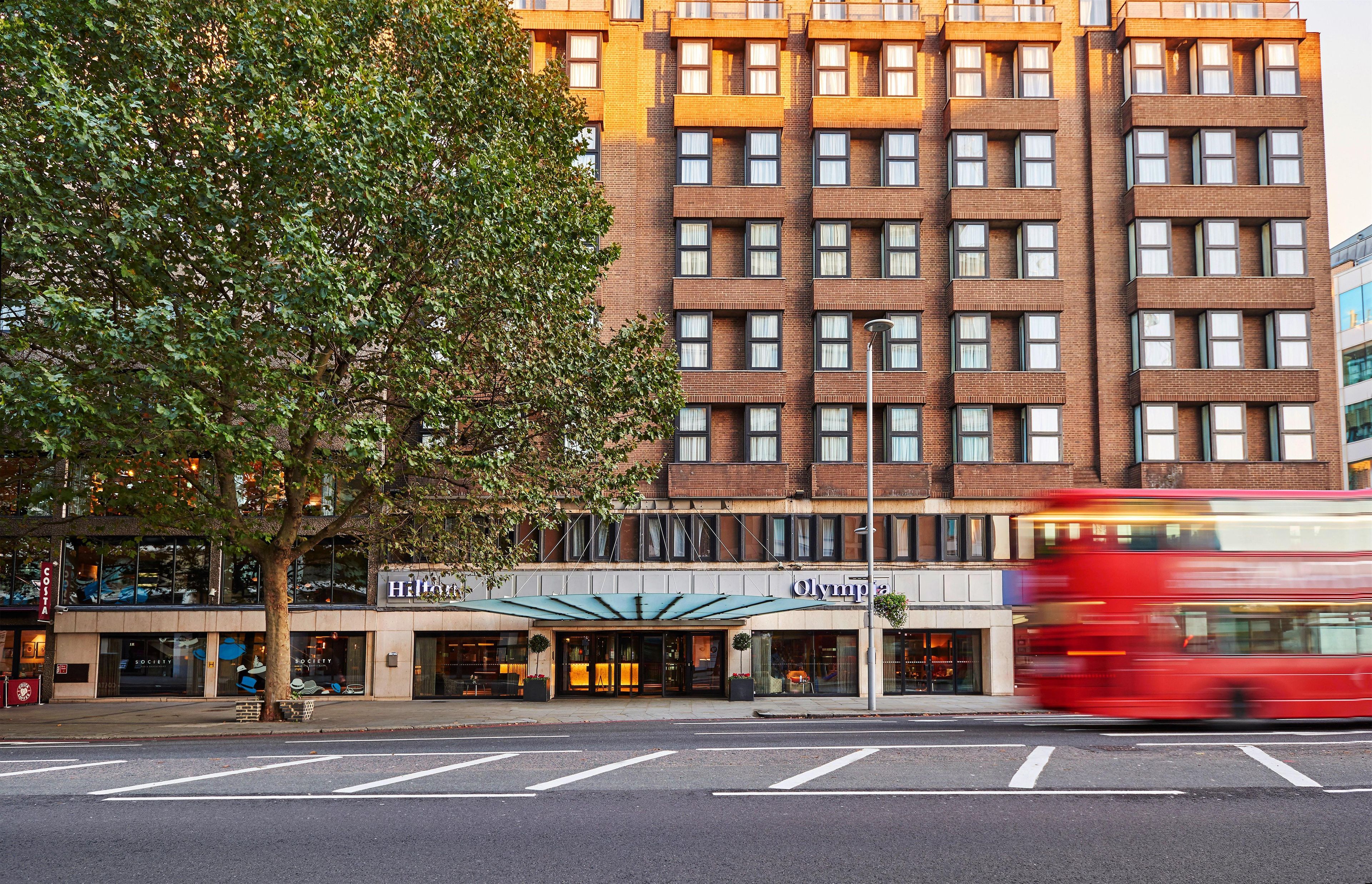 Un hotel con fachada moderna, varios pisos y un árbol frente a él.