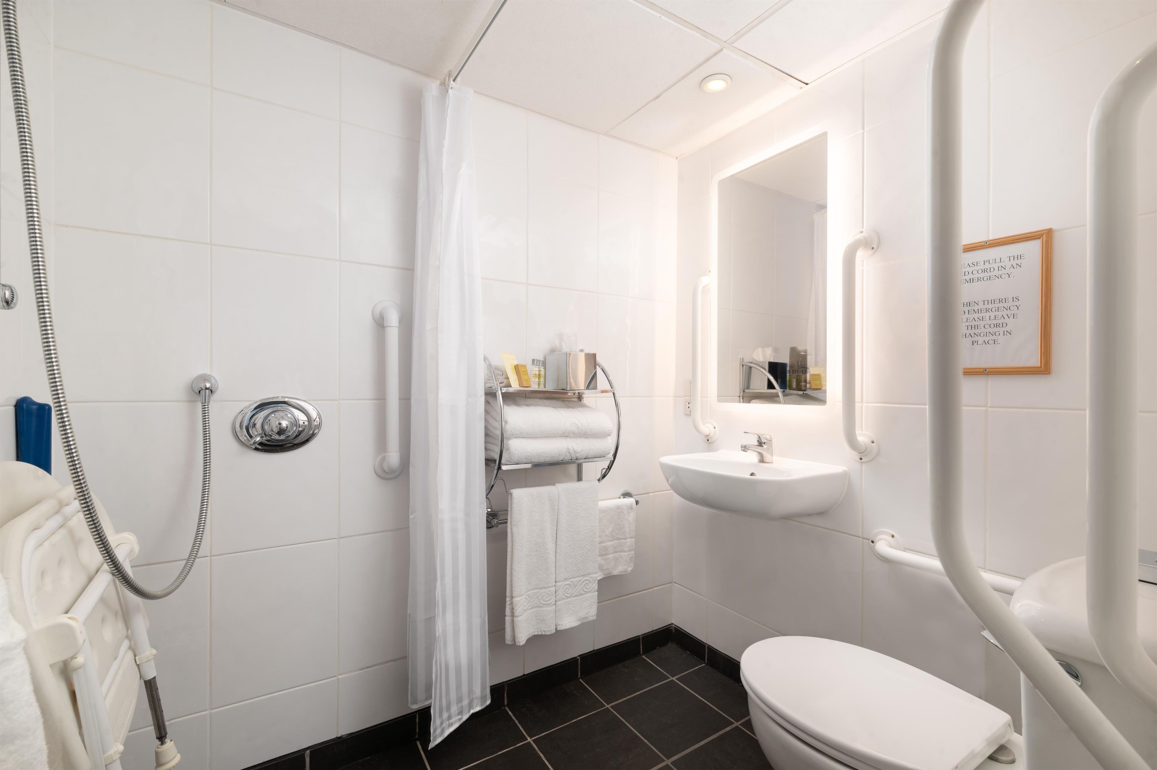 A bathroom with a shower, toilet, sink, and towel rack.
