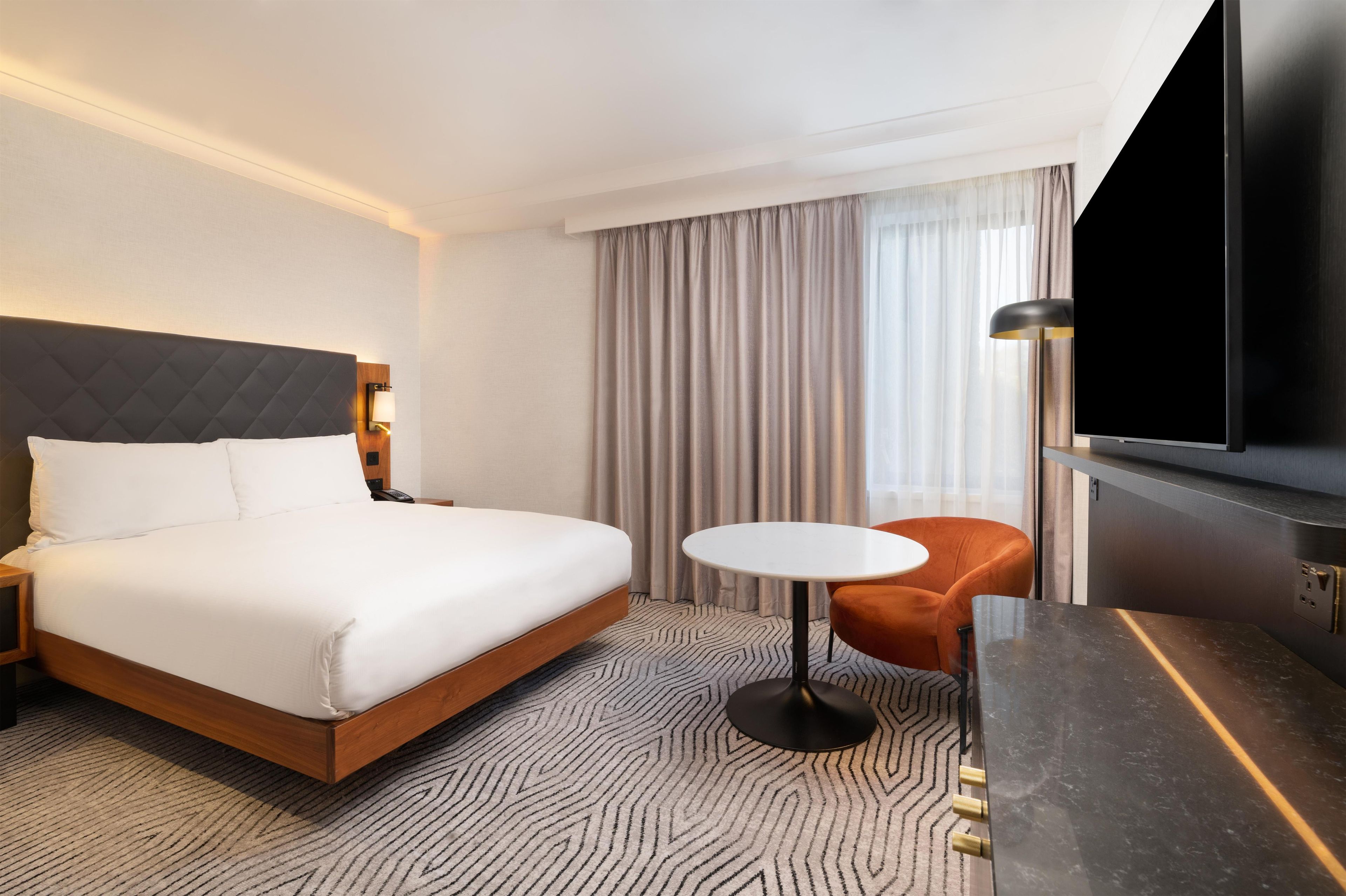 A hotel room with a bed, a round table, a TV, and a chair.