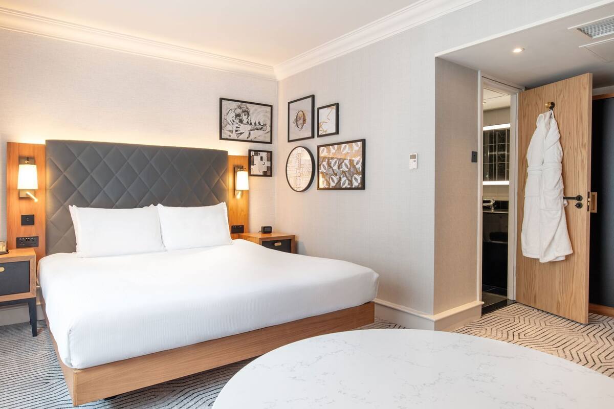 A hotel room with a large bed, bedside tables, a wardrobe, and artwork on the walls.