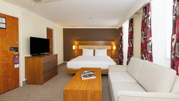 A hotel room with a bed, a television on a wooden dresser, a coffee table, and a sofa.