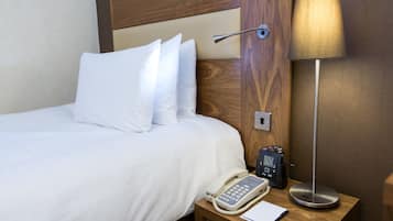 A hotel room with a bed, a bedside table with a lamp, a phone, and a notepad.
