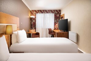 A hotel room with a bed, a desk, a chair, a television, and a window with curtains. - Hilton London Olympia (London)