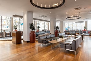 A spacious lounge area with leather sofas, wooden tables, and large windows providing natural light. - Hilton London Olympia (London)