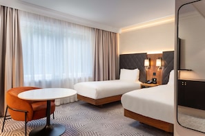 Two single beds with tufted headboards, a small table, and a comfortable armchair.