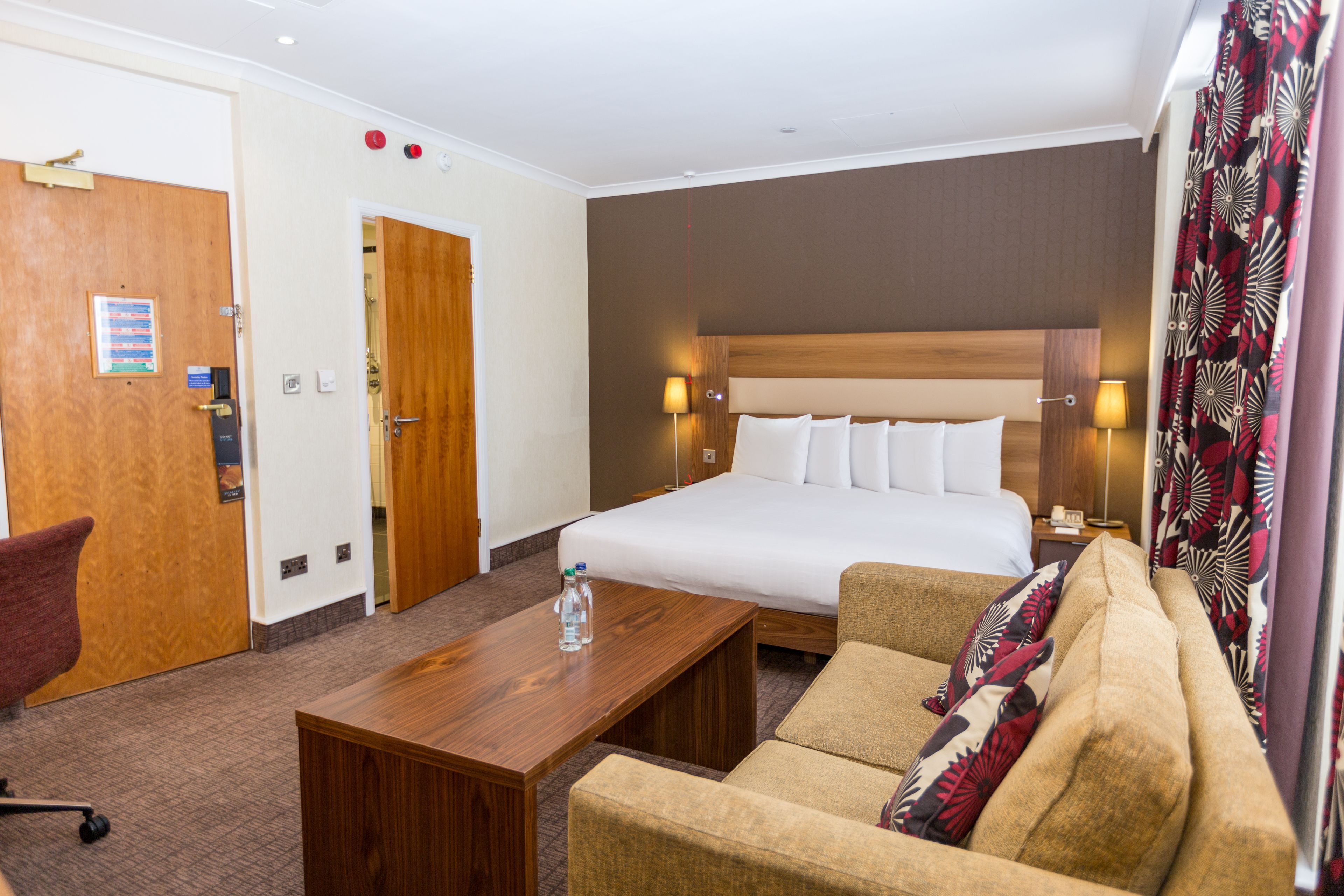 A hotel room with a large bed, a wooden desk, a sofa, and a door.