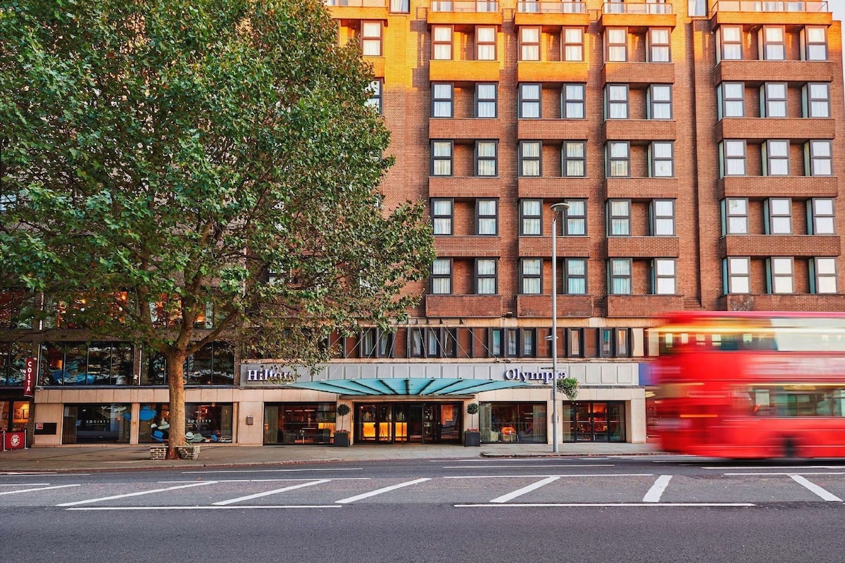 A hotel with a brick facade, storefronts, and a tree in the foreground.
