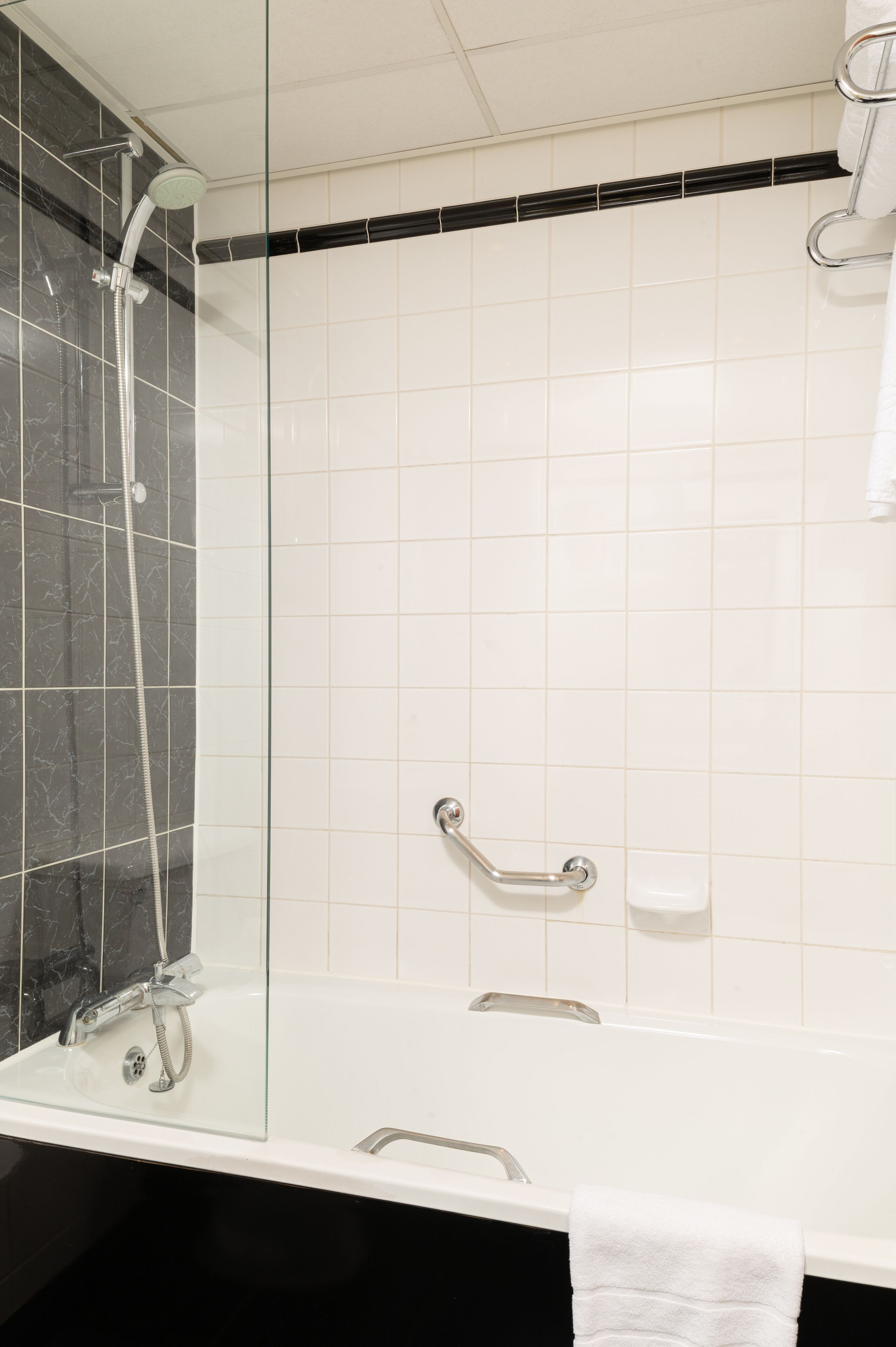 Un baño moderno con ducha de vidrio, bañera blanca y pared revestida de baldosas negras.