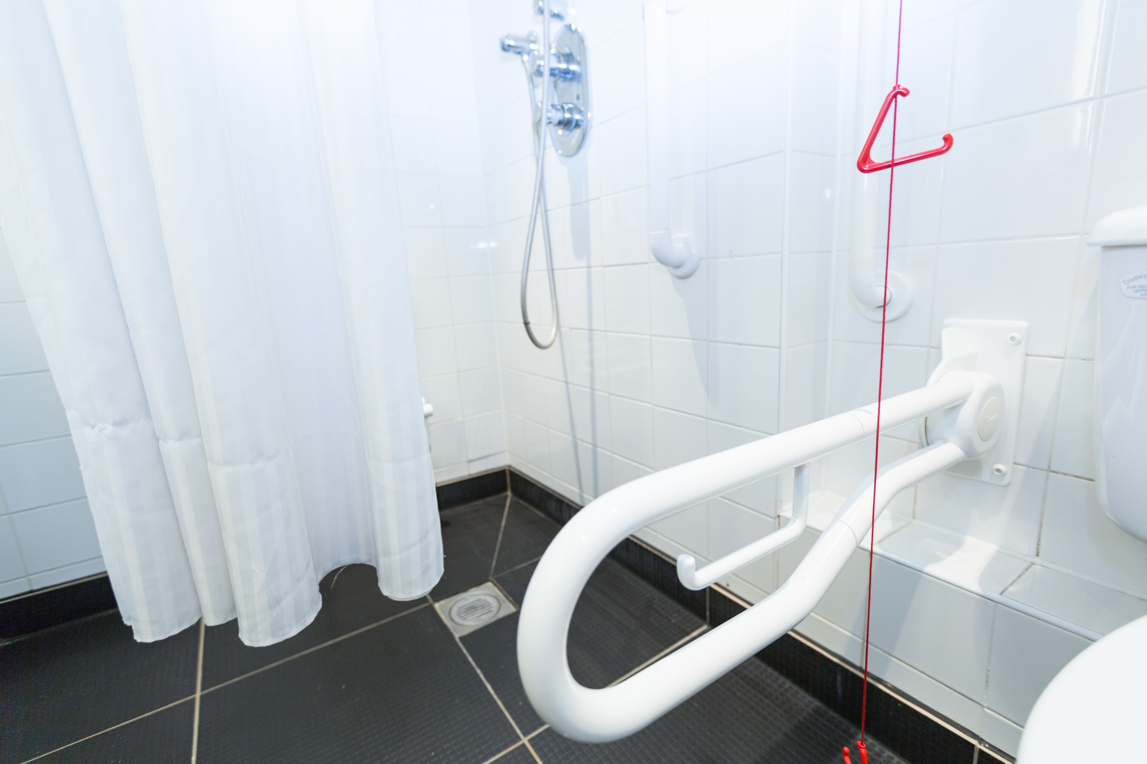 Een badkamer met een wit toilet, een douche met een chroomdouchekop en een witte handdoekhouder.