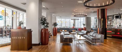 A modern lounge area with wooden flooring, leather sofas, and a reception desk labeled 'SOCETY'.