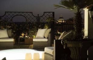 A rooftop lounge area with wicker furniture, a pool, and a view of a building with a dome.