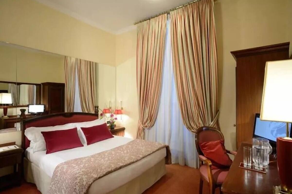 A hotel room with a bed, a desk with a computer, a chair, and curtains.
