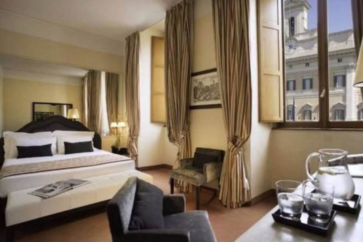 A hotel room with a bed, a chair, a table with glasses and a pitcher, and curtains.