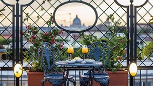 Una mesa con sillas y bebidas, un espejo y una vista de un edificio tras una verja metálica.