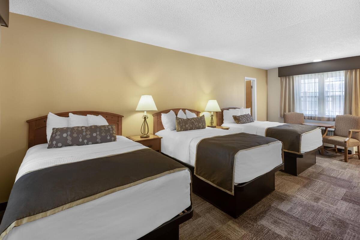 A hotel room with three beds, a desk, and a chair.