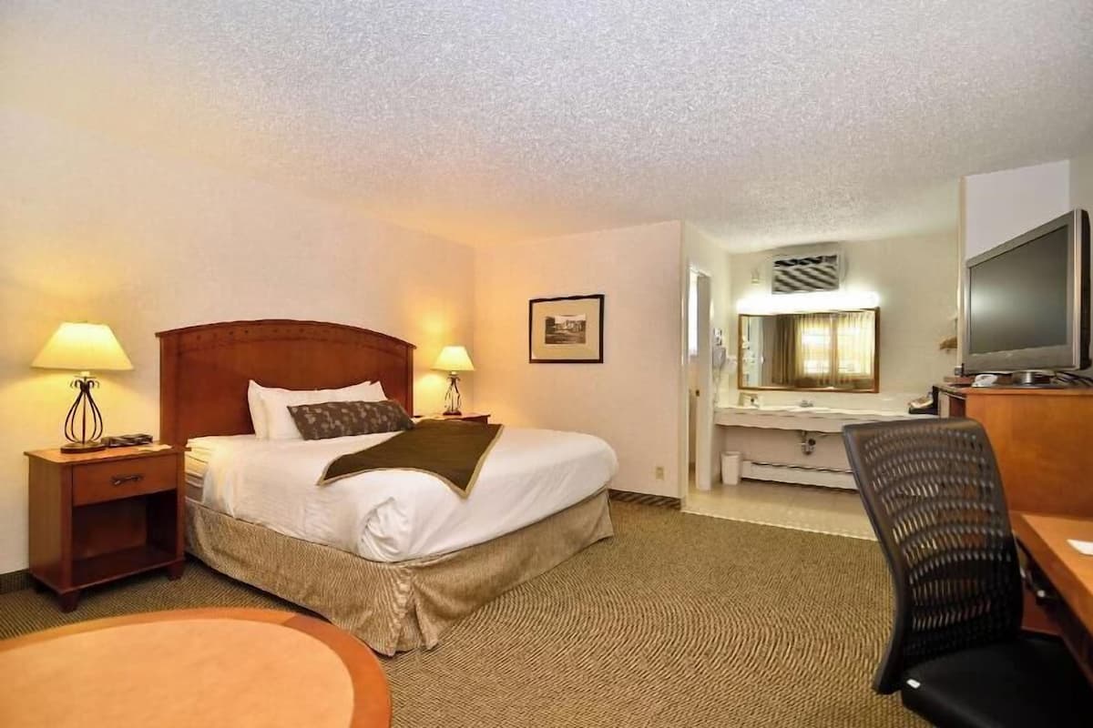A hotel room with a bed, two bedside lamps, a desk with a chair, a TV, and a bathroom mirror.