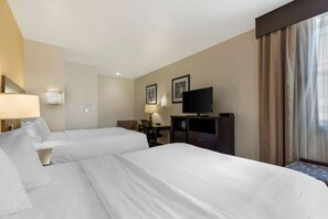 Ein Hotelzimmer mit zwei Betten, einem Schreibtisch, einem Sessel, einem Fernseher und einem Fenster mit Vorhängen.