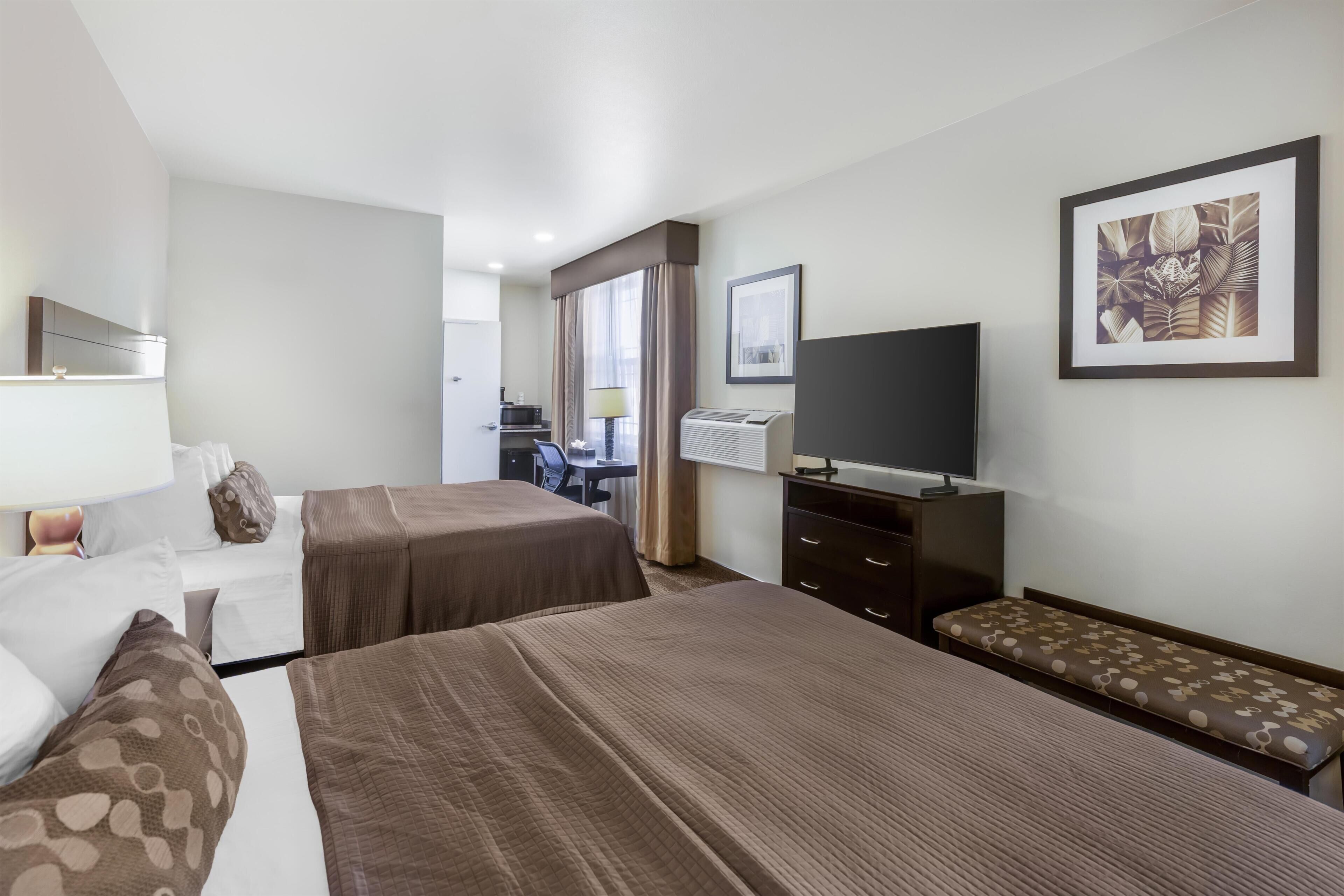 A hotel room with two beds, a desk, a television, and a framed picture on the wall.