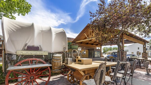 Un espace extérieur aménagé dans un style rustique, avec une table et des chaises en bois, un chariot couvert et un panneau indiquant : « Bienvenue à notre centre de bien-être. »