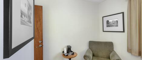 A room with a wooden door, a framed picture on the wall, a small table with a coffee maker, and a green armchair.