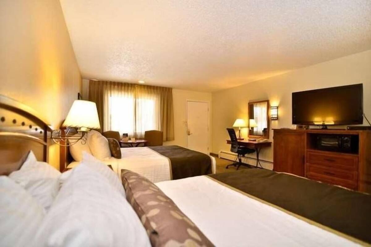 A hotel room with two beds, a desk, a chair, a television, and a wardrobe.
