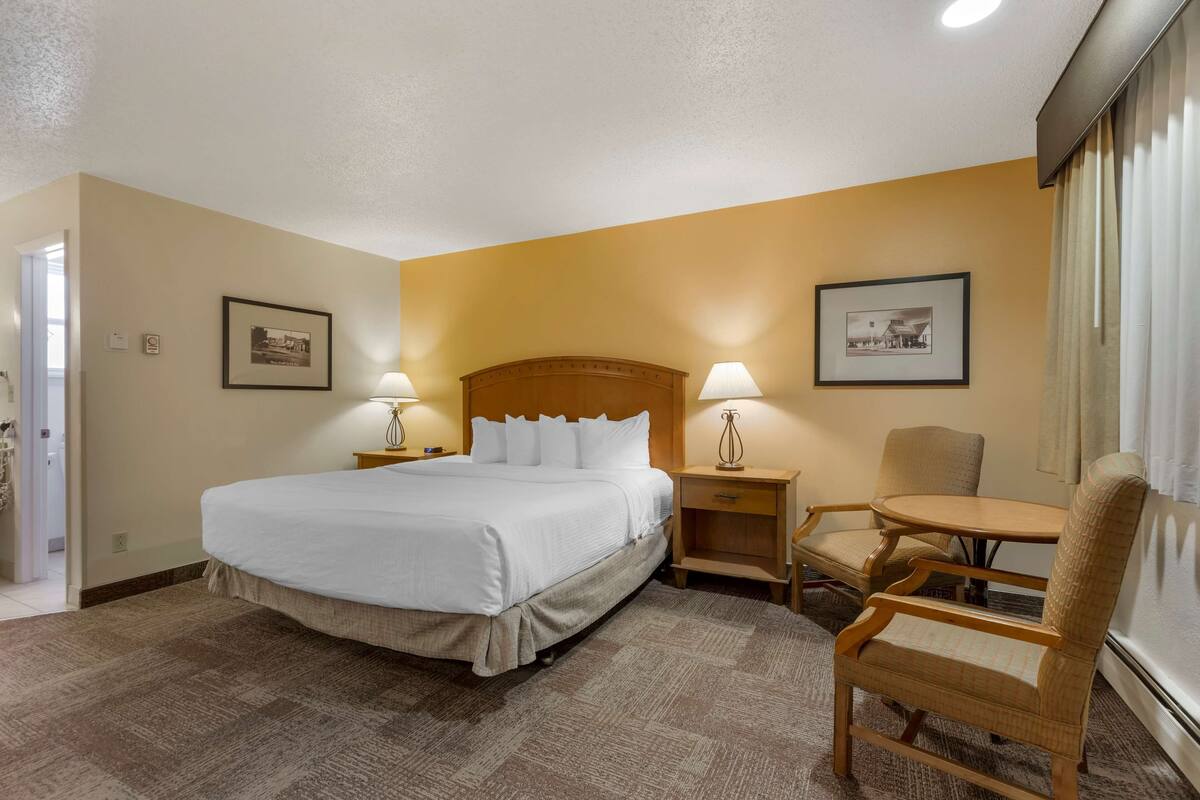 A hotel room with a large bed, two bedside tables with lamps, a chair, and two framed pictures on the walls.
