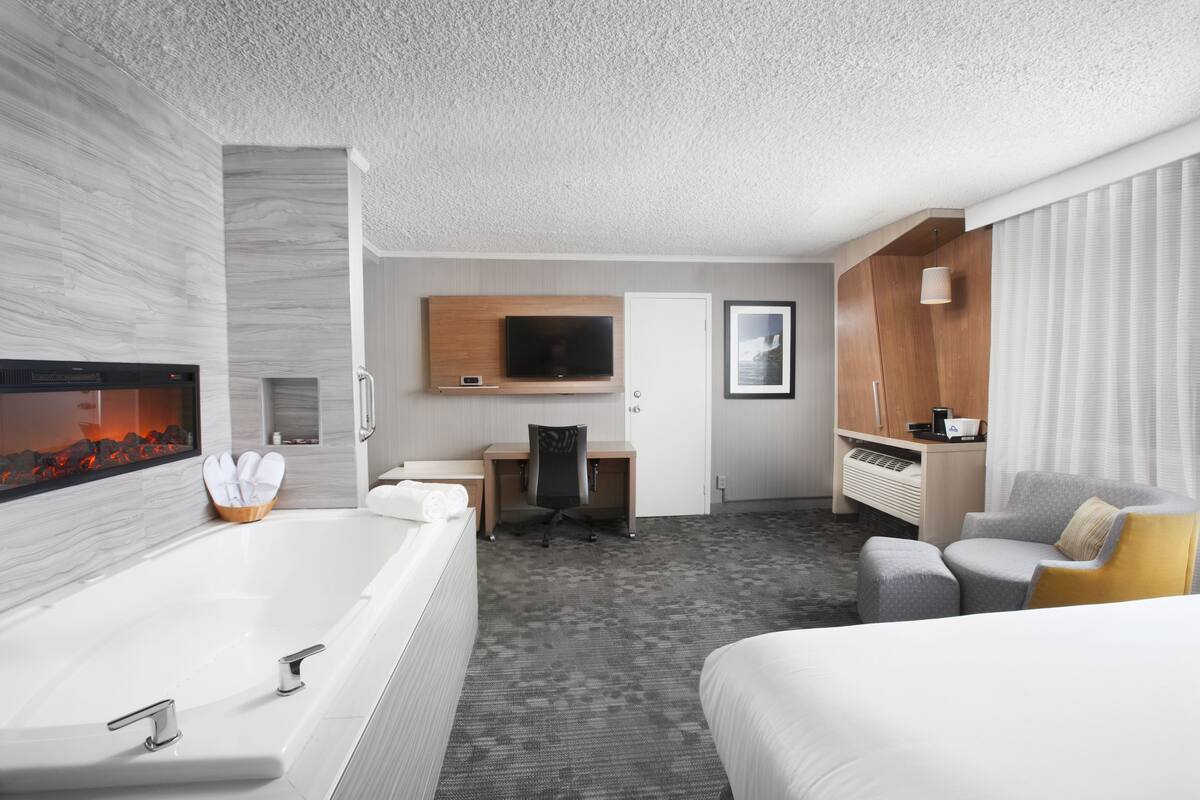 A hotel room with a large bathtub, a desk with a chair, a bed, and a television mounted on the wall.