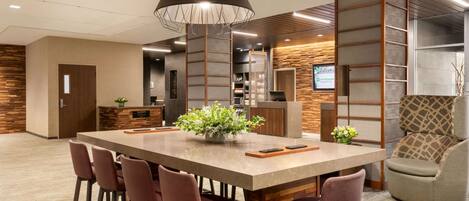 Un comedor moderno con una gran mesa rectangular, seis sillas, una planta central y una lámpara colgante original.
