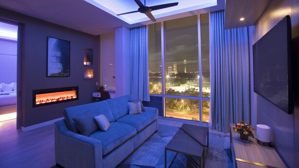 Un salón moderno con sofá, mesa de centro, chimenea y un amplio ventanal con vistas a la ciudad.