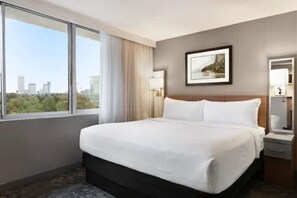A hotel room with a large bed, a window with a city view, a framed picture on the wall, and a bedside table with a lamp. - Wyndham Garden at Niagara Falls (Niagara Falls)