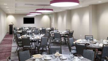 A conference room with multiple tables set for dining, equipped with chairs, plates, glasses, and cutlery.