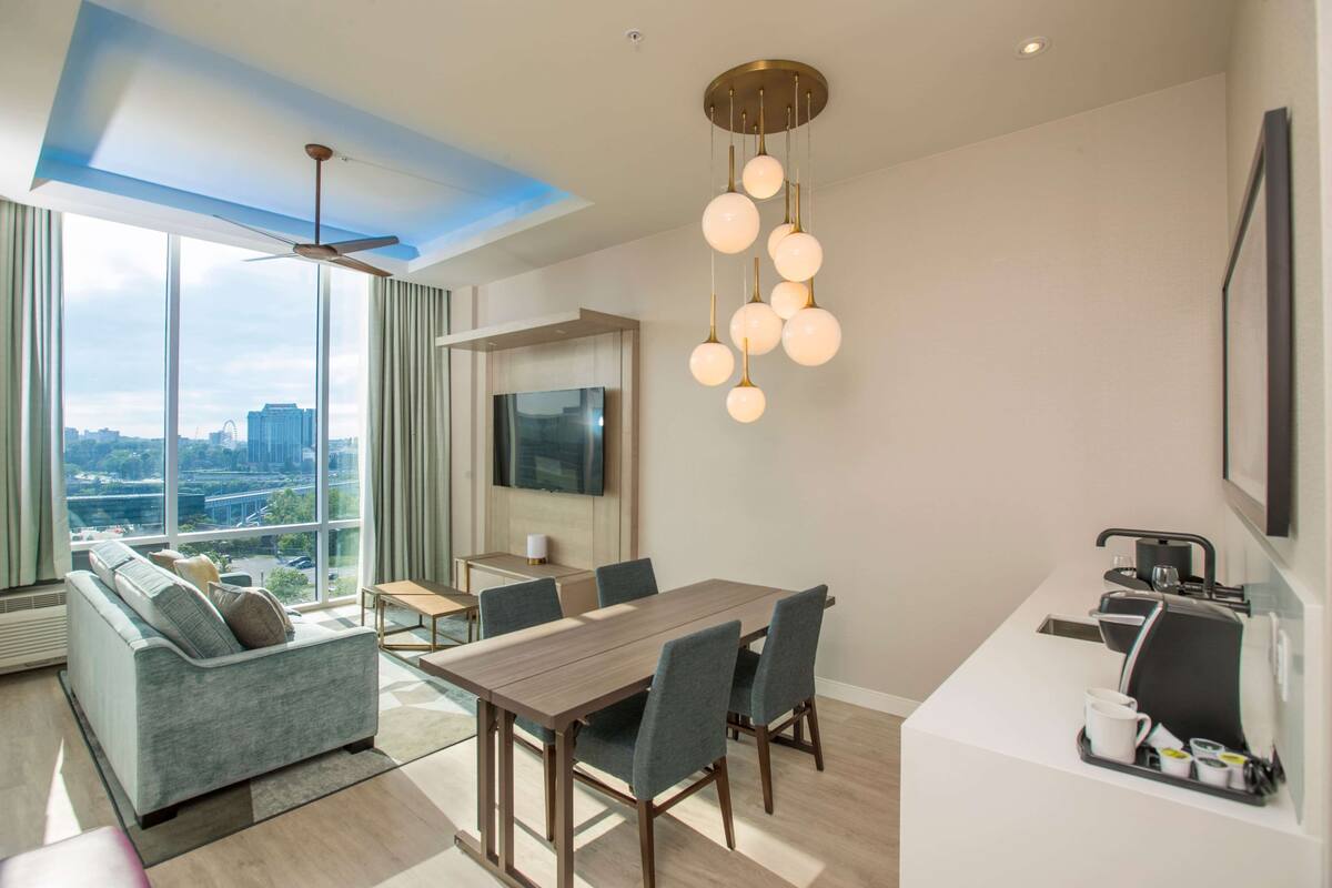 A modern hotel room with a dining area, a sofa, a TV, and a coffee machine.