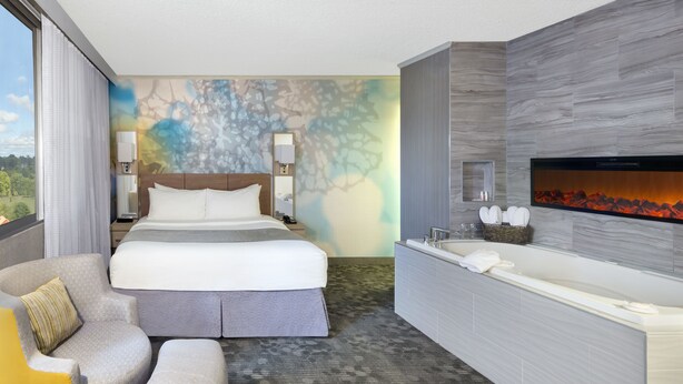 A modern hotel room with a large bed, a sitting area, a bathtub, and a wall-mounted TV. - Wyndham Garden at Niagara Falls (Niagara Falls)