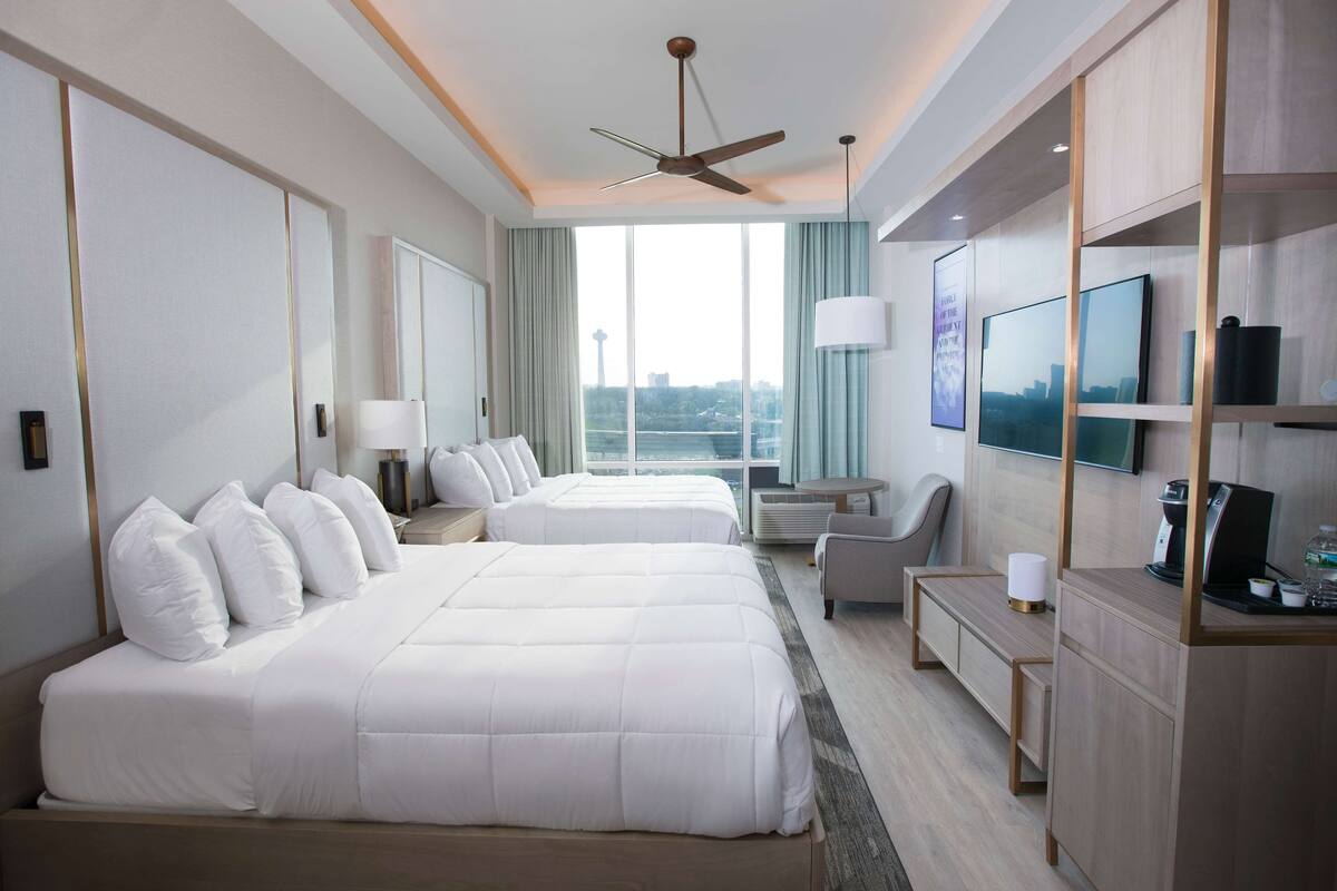 A hotel room with two beds, a desk, a chair, a TV, and a city view.