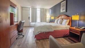 Quarto de hotel com cama, escrivaninha, cadeira e janela com cortinas.